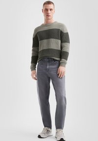 Sweter wełniany z poziomymi paskami w ciemnozielonym i szarym kolorze, zestawiony z szarymi dżinsami i białymi trampkami. Struktura ściągacza, luźny krój.