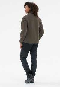 Fleece jacket in olive green with a smooth upper, paired with black pants and gray hiking boots. Features a high collar and relaxed fit.