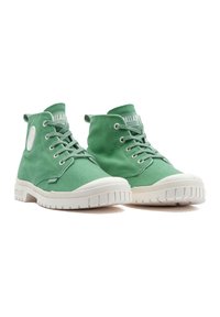 Grüne Canvas Hochtop-Sneaker mit weißen Gummisohlen, ausgestattete mit metallischen Ösen, flachen Schnürsenkeln und einem runden Logopatch an der Seite.