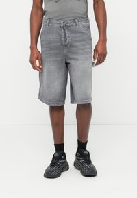 Shorts di jeans grigi con un taglio classico, dotati di chiusura con bottoni e una sottile texture slavata. Abbinati a sneakers nere e calzini.