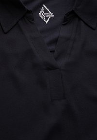 Polo shirt nera con un tessuto texture, presenta un colletto, un'apertura a v e un piccolo logo bianco sul lato superiore sinistro.