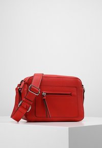Červená kožená taška přes rameno s obdélníkovým tvarem, nastavitelným popruhem, přední kapsou na zip a texturovaným povrchem.