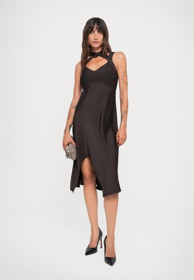 Zwarte mouwloze jurk met een halternek, uitsnijding, asymmetrische zoom, gladde textuur, gecombineerd met een getextureerde clutch en puntige hakken.