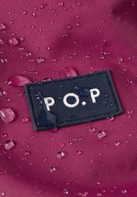 Vedenkestävä violetti kangas, jossa on vesipisaroita, ja teksturoitu tummansininen etiketti, jossa on valkoiset kirjaimet "P.O.P.".