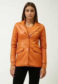 Blazer de cuero sintético naranja con solapa muesca, cierre de doble botón y dos bolsillos frontales. Presenta un suéter naranja acanalado debajo.