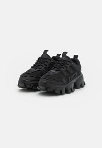 Ein Paar klobige schwarze Sneakers mit dicken strukturierten Sohlen, Schnürungen und Zuglaschen vor einem schlichten weißen Hintergrund.