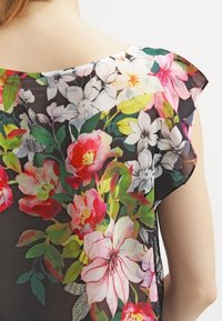 Blomstret bluse med en sort gennemsigtig baggrund, der har levende pink, røde og hvide blomster. Korte ærmer, afslappet pasform, delikat tekstur.