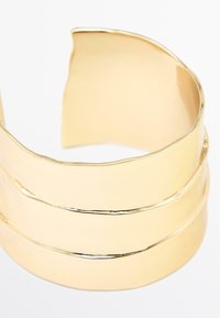 Bracelet en or avec trois bandes ondulées. Texture lisse et finition brillante, avec un bord légèrement irrégulier pour un détail unique.