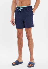 Bañador de marina con cintura ajustable mediante cordón y acentos en azul claro. Cuenta con bolsillos laterales y un logotipo en el muslo izquierdo.
