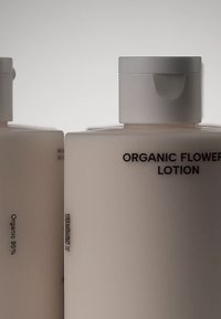 Biała, nieprzezroczysta butelka z emulsją z okrągłą zakrętką, oznakowana etykietą "Organiczny Lotion Kwiatowy" oraz "Organiczny 95%" w czarnym tekście, o gładkiej fakturze.