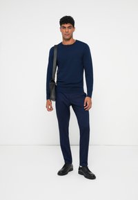 Suéter de malha azul-marinho, com gola redonda, combinado com calças a condizer. Sapatos de couro pretos e uma bolsa messenger completam o visual. Design simples e coeso.