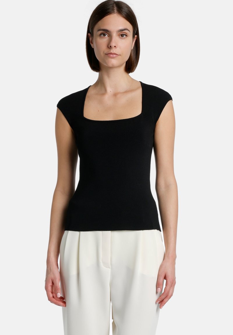 Top negru cu mansete scurte, cu decolteu pătrat, dintr-un material neted, cu un design ajustat, asortat cu pantaloni de culoare deschisă.