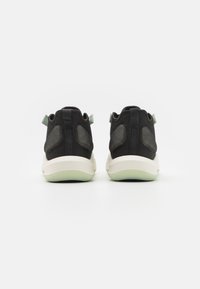 Ett par svarta mesh-sneakers med vita sulor och ljusgröna dragremmar, vy från baksidan på en enfärgad vit bakgrund.