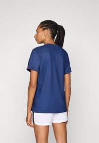 Navy athletic shirt with a round neck, short sleeves, and textured fabric. Paired with white shorts, showing a streamlined design.