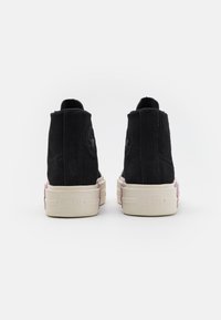 Czarne zamszowe sneakersy typu high-top z masywną kremową podeszwą, z wyraźnym logo z tyłu oraz detalami szycia.