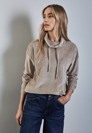 Beige cowl-neck sweatshirt i mjukt tyg med långa ärmar, i kombination med mörkblå jeans. Har snodd med silverfärgade ändar.