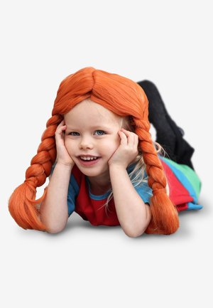 Glimlachend jong kind liggend op de buik, gekleed in een kleurrijke outfit en een feloranje pruik met twee lange gevlochten staartjes.