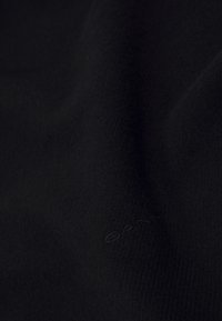 Sort strikstof med en blød tekstur, der har et diskret GANT-logo prægede i materialet. Glat overflade med et ensartet mønster.