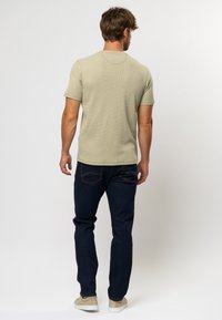 Cămașă ajustată, cu mânecă scurtă, de culoare verde deschis texturată, asociată cu blugi de culoare albastru închis; blugii au un design clasic cu cinci buzunare și cusături subtile.
