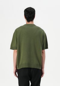 Green knitted short-sleeve sweater with a ribbed neckline and hem, featuring a relaxed fit and smooth texture.