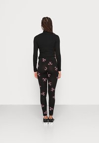 Leggings noirs avec un motif de canne en sucre rouge et blanc. Portés avec un haut noir à manches longues et des baskets noires avec des accents blancs.