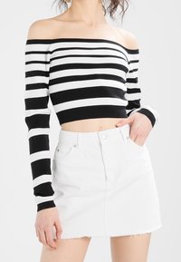 Schwarz-weißer gestreifter schulterfreier, gerippter Cropped-Top kombiniert mit einem hoch taillierten weißen Denim-Rock mit rohem Saum.