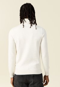 Suéter de cuello alto color crema en tejido de punto suave; cuenta con mangas largas, puños acanalados y un diseño ajustado en la cintura.