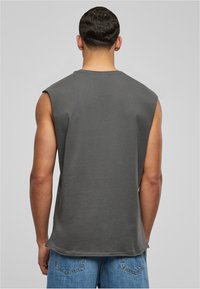 T-shirt sans manches gris avec une coupe décontractée, fabriqué en coton. Le dos présente un col rond et une texture lisse, associé à un jean bleu.