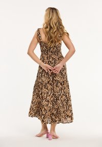 Vestido largo sin mangas de patrón marrón y beige, con tirantes con volantes y corpiño fruncido. Combinado con sandalias rosas de tacón grueso.