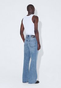 Jeans de mezclilla de color azul claro y pierna ancha, con cintura alta, bolsillos traseros y una etiqueta de marca en la cintura. Llevados con una camiseta sin mangas blanca.