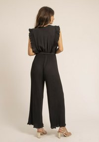 Combinaison noire côtelée avec un décolleté froncé et des jambes larges. Le tissu a une texture lisse et présente une taille cintrée pour souligner la silhouette.