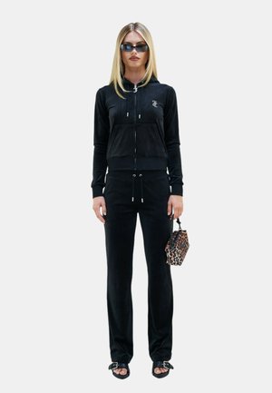 Tuta in velluto nero con felpa con zip e pantaloni con coulisse, abbinato a una borsa con stampa leopardata e sandali neri con tacco. Tessuto con texture.