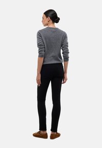 Pull en tricot gris à manches longues, col rond, associé à un jean noir près du corps et des chaussures en suedine marron. Design simple et classique.