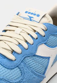 Sneaker blu con materiali in rete e suede, accenti bianchi, modelli testurizzati, lacci bianchi piatti e un logo sulla linguetta.