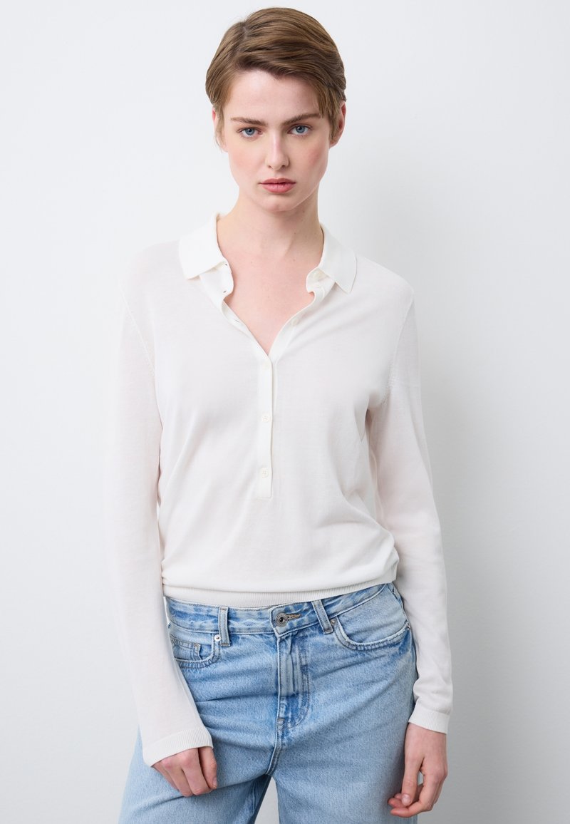 Weißes Langarmhemd mit einem Button-Down-Kragen und einer dezenten Struktur, kombiniert mit hellblauen hoch taillierten Jeans.