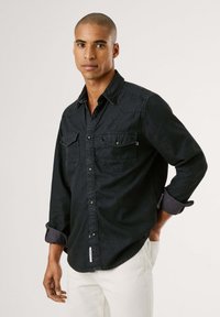 Dunkelblausse Shirt mit langen Ärmeln, zwei Brusttaschen, Knopfleiste und hochgerollten Manschetten. Saubere, einfarbige Optik mit subtiler Textur.