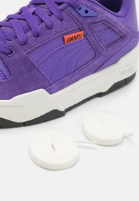 Lilla ruskind- og lædersneaker med hvide såler og snørebånd. Har et rødt "GNAP!" mærke og markante designlinjer på siden.