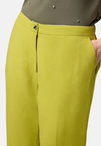 Pantalons vert clair en tissu texturé, dotés d'une taille avec fermeture à bouton devant et de poches latérales.