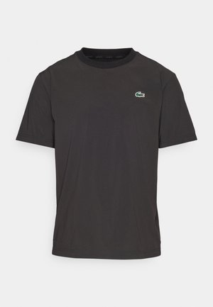 Črna majica s kratkimi rokavi iz mehkega materiala, ki ima okroglo ovratnico in majhen zeleni krokodilov logotip na levem prsnem delu.