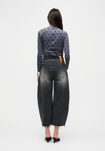 Γκρι μακρυμάνικο τοπ με πουά, δεμένο στο πίσω μέρος, συνδυασμένο με μαύρο τζιν φαρδιάς γραμμής με ξεθωριασμένη υφή και σκισμένο τελείωμα. Μαύρα σανδάλια με τακούνι.