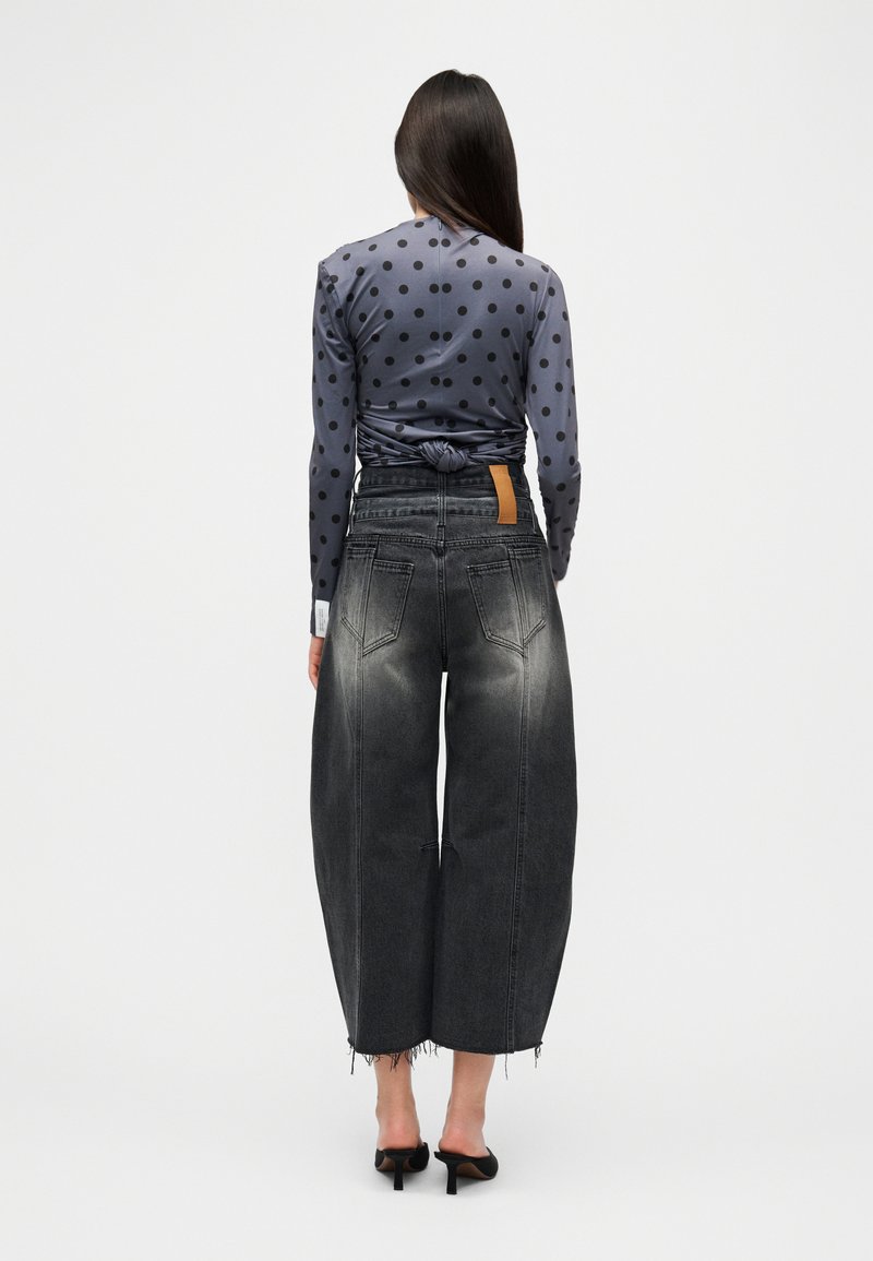 Haut à manches longues gris à pois, noué à l'arrière, associé à un jean noir à jambes larges avec une texture délavée et un ourlet effiloché. Sandales noires à talons.