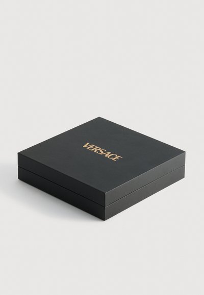 Črn pravokotni škatla z gladko teksturo, opremljena z zlatim logotipom "VERSACE" na vrhu. Oblikovanje je minimalistično in elegantno.
