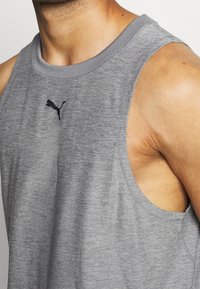 Šedý bezrukávový atletický tílko vyrobené z texturované tkaniny, s černým logem Puma na hrudi a klasickým kulatým výstřihem.