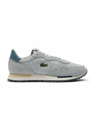 Sneaker gri cu partea superioară din suede și plasă, talpă intermediară albă și talpă exterioară din cauciuc negru. Prezintă un logo brodat verde și un accent teal la călcâi.