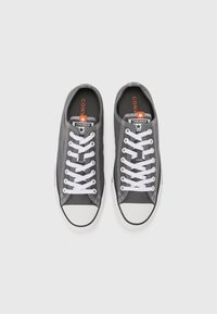 Gray canvas sneakers with white rubber toe caps and laces. Features a black and white stitching pattern and orange logo on the tongue.