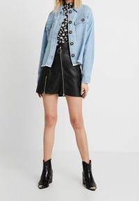 Světle modrá džínová bunda s knoflíkovým zapínáním, spárovaná s černou koženou sukní s předním zipem. Černé kotníkové boty dotvářejí vzhled.