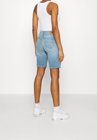 Shorts de mezclilla en azul claro con un acabado limpio, con cintura alta y dos bolsillos traseros. Combinados con una camiseta ajustada blanca y zapatillas.