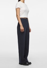 Vit kortärmad crop top i kombination med högmidjade marinblå ränderade byxor. Byxorna har en lös passform och är tillverkade av ett strukturerat material. Svarta skor.