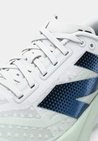 White athletic shoe with a textured mesh upper, blue triangular pattern accents, flat laces, and a cushioned sole.