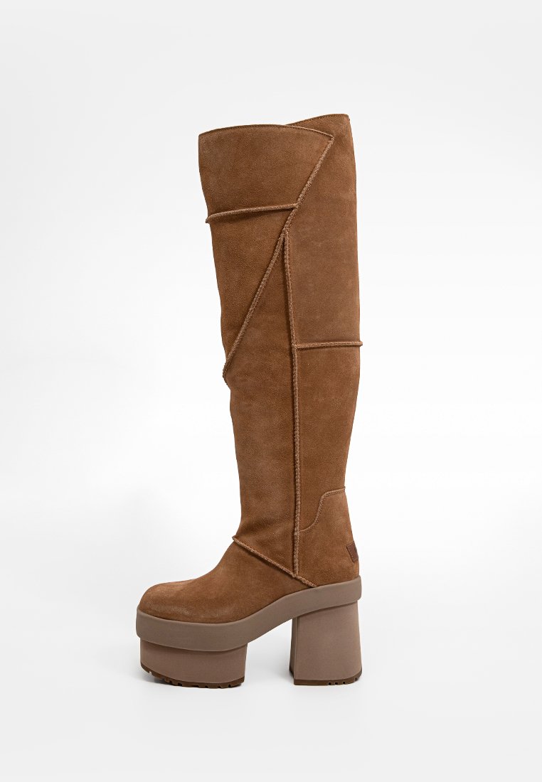 Bottes marron, jusqu'aux genoux, en daim avec un talon plateforme épais. Présente des coutures texturées et un design géométrique sur le dessus.